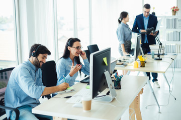 Attractive business people in headsets are smiling while working with computer in modern office