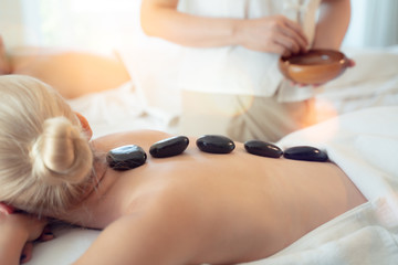 beautiful girl relaxes with traditional hot stones along the spine at spa and wellness center.Young caucasian woman with perfect skin,facial massage,skin care,treatment.Spa and massage concept.