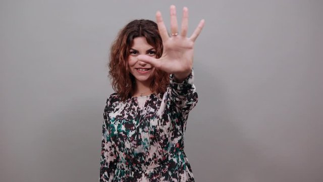 Cheerful charming young lady over isolated gray background in fashion shirt showing six fingers at camera, smiling, having nice ring. People emotions. Lifestyle concept
