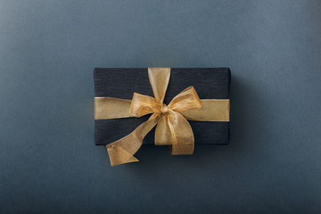 a gift wrapped in black paper and tied with a gold ribbon. expensive gift concept.
