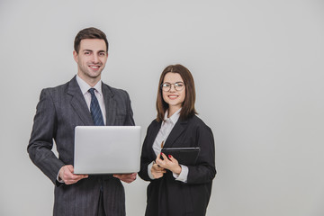 Young business couple standing, using digital tablet and laptop together, smiling.