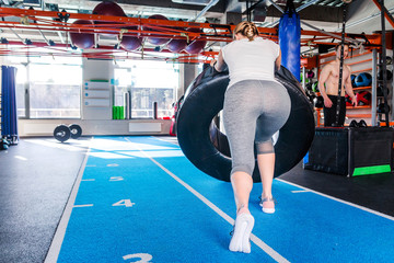 Fototapeta na wymiar Fit female athlete working out with a huge tire, turning and flipping in the gym.