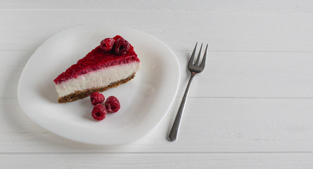 Cheesecake slice with raspberries on white table. 