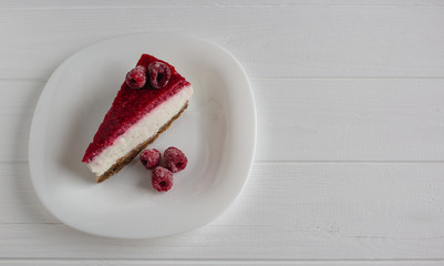 Cheesecake slice with raspberries on white table. 