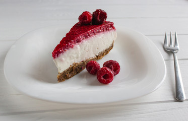Cheesecake slice with raspberries on white table. 