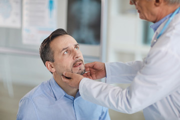 Mature male patient sitting and looking at doctor while he examining him during medical exam at hospital