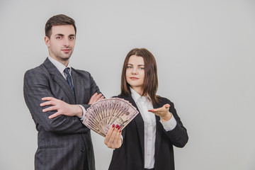 Rich confident business couple. Man is standing with his hands folded. Woman on his side is extending a fan of dollar banknotes.