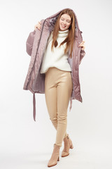 Beautiful sexy pretty girl with long brown hair and perfect body weared in beige leather pants and white sweater, jasmine down jacket, boots. Isolated on white background.