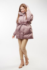 Beautiful sexy pretty girl with long brown hair and perfect body weared in beige leather pants and white sweater, jasmine down jacket, boots. Isolated on white background.