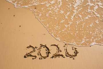 Summer beach holiday 2020 season golden sand - year - decade - new season lettering on the beach with wave and clear blue sea. Numbers 2020 year on the sea shore, message handwritten New Years concept