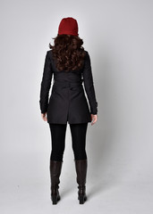 full length portrait of a pretty brunette girl wearing a black coat, leather boots and red beanie....
