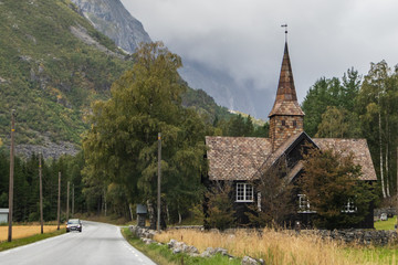 Fototapeta na wymiar Old wooden black wood church in the mountains of Norway. Scandinavia rural countryside landscape