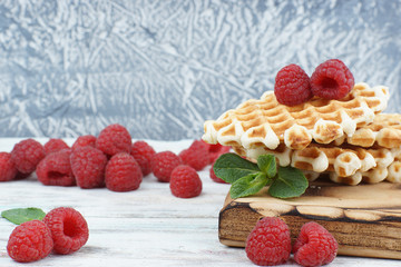 A stack of sweet baked waffles and large raspberries on a table