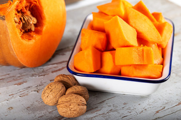 Peeled and chopped pumpkin and walnuts on wooden background.