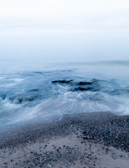 Calm waves rolling in on a beach at Gotland during winter. Typical pale winter light over the horizon.