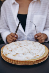 Tasty lemon meringue pie. Traditional french sweet pastry tart. female with fork and knife sits at table opposite big cake and plans to eat it completely