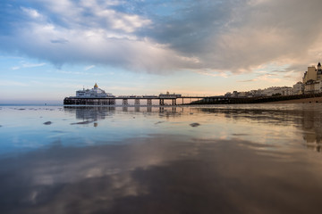 Obraz premium Eastbourne beach at low tide with wet reflective sand and the pier in the background.