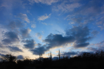 Evening landscape with colorful clouds and bright blue sky against a darkening forest.