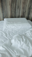Single bed with white linens and duvets that are used and crumpled.