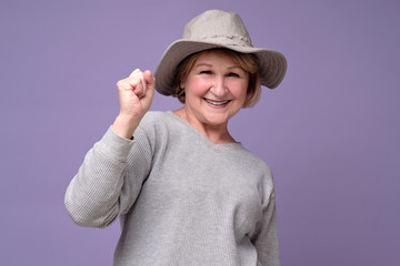 Senior woman wearing summer hat smiling holding fist up. Studio shot