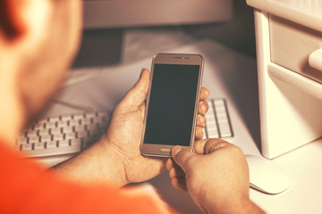 Jeune homme utilisant un téléphone portable devant un ordinateur