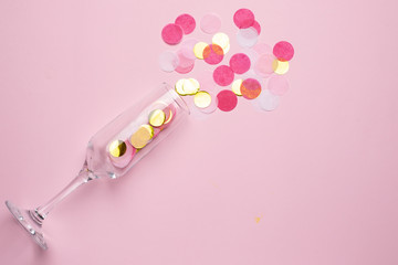 Champagne glass with golden and pink confetti on pink color paper background minimal style