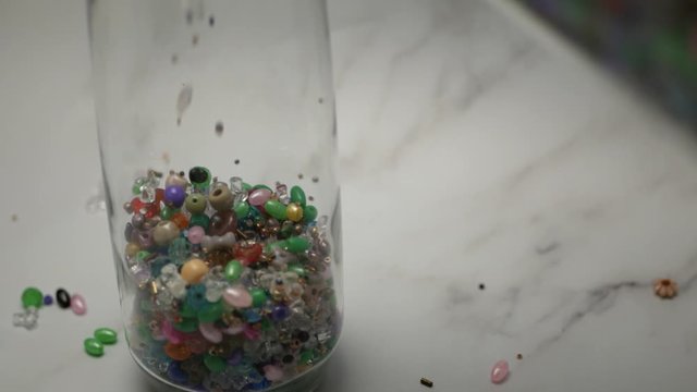 Assorted Beads Pour Into Clear Glass Container