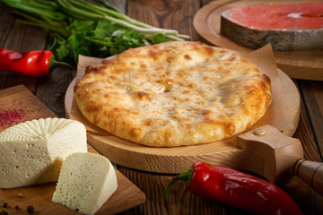 Round meat pie. A traditional dish of Caucasian cuisine. The ingredients are on the table: fish, herbs, spices, cheese and bell peppers. Cooked in the oven. The concept of diet and healthy eating.