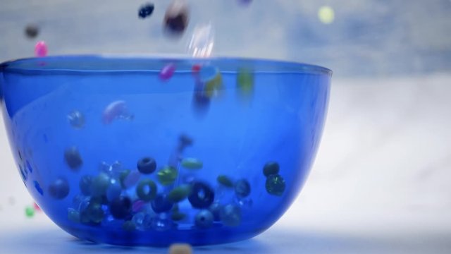 Assorted Beads Pour Into Side View of Blue Bowl