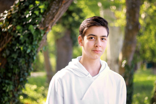Portrait of handsome shy teenager boy in park outdoors. Natural light. Adolescent boys