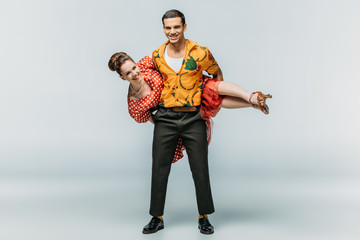 cheerful man holding woman while dancing boogie-woogie on grey background
