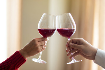 A cheerful young couple crossing their wineglasses at a restaurant. A man and his girlfriend drinking wine at a cafe. Red rose on a table. Valentine's day concept.