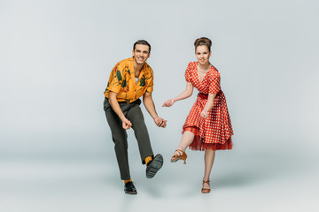 cheerful dancers looking at camera while dancing boogie-woogie on grey background