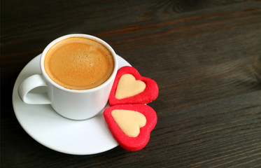 One cup of hot coffee with two heart shaped cookies on dark brown wooden table