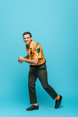 handsome, stylish dancer looking at camera while dancing boogie-woogie on blue background