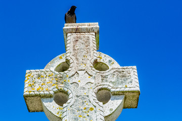 Black bird on old stone celtic cross on a bright clear blue sky background