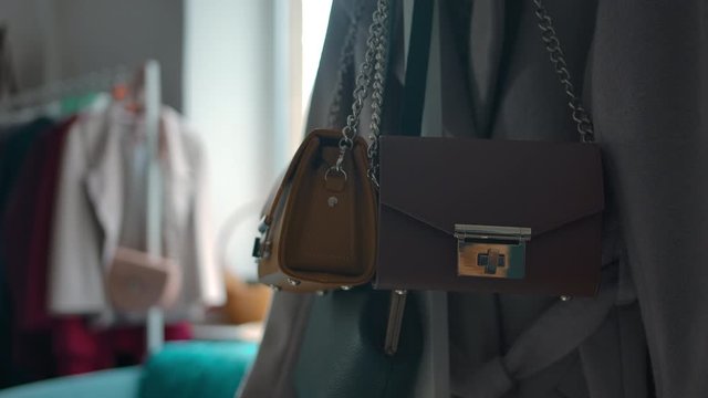 Pan right and zoom in of fashionable brown leather female handbag with metal clasp and chain hanging in fashion boutique.