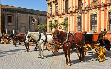 Fototapeta na wymiar Horse carriages and Archbishop's Palace in the Virgin of the Kings (Virgen de los Reyes) Square in Seville, Andalusia, Spain
