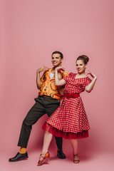 elegant dancers looking at camera while dancing boogie-woogie on pink background