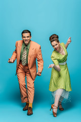 smiling dancers looking at camera while dancing boogie-woogie on blue background