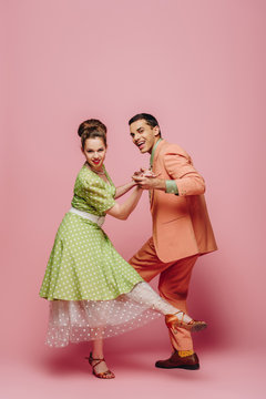 elegant dancers holding hands while dancing boogie-woogie on pink background