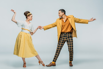 Stylish dancers holding hands while dancing boogie-woogie on grey background