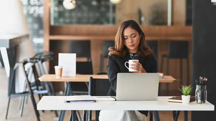 Shot of a confident woman holding a coffee cup while working in front of computer.