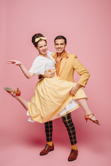 smiling dancer holding girl while dancing boogie-woogie on pink background
