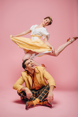 cheerful man sitting on floor and happy girl jumping while dancing boogie-woogie on pink background