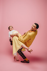 cheerful couple looking at camera while dancing boogie-woogie on pink background