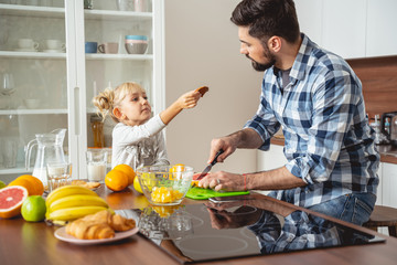 Adorable little girl giving father delicious cookie