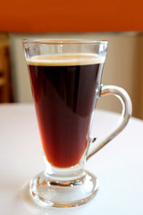 Hot black coffee in a transparent glass served on white table