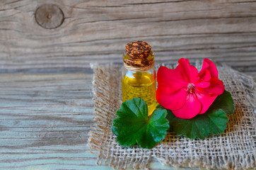 Geranium essential oil in a glass bottle with flower and leaf of the geranium plant on wooden...