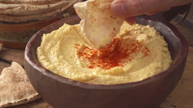 Hand dipping a pita chip into a delicious bowl of hummus.